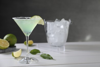 Delicious Margarita cocktail in glass and limes on white wooden table, space for text