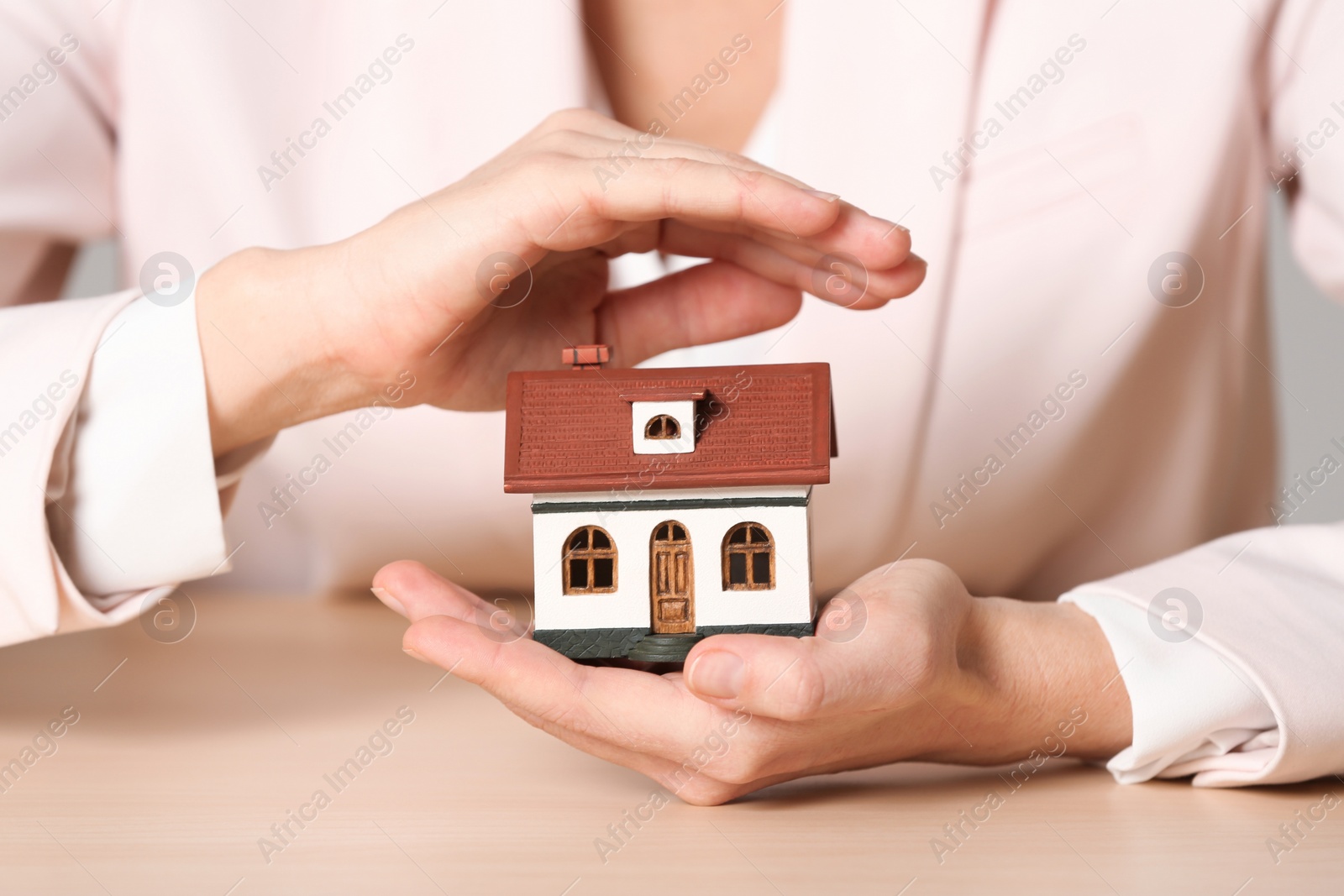 Photo of Female agent covering house model at table, closeup. Home insurance