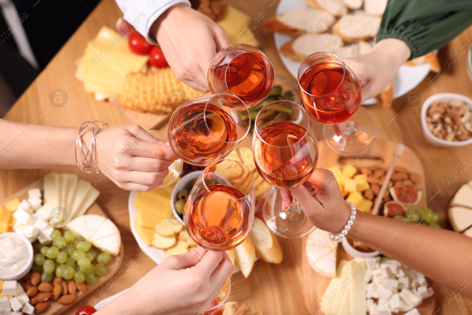 Photo of People clinking glasses with rose wine above wooden table, closeup