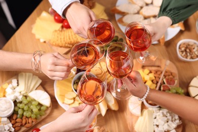 Photo of People clinking glasses with rose wine above wooden table, closeup