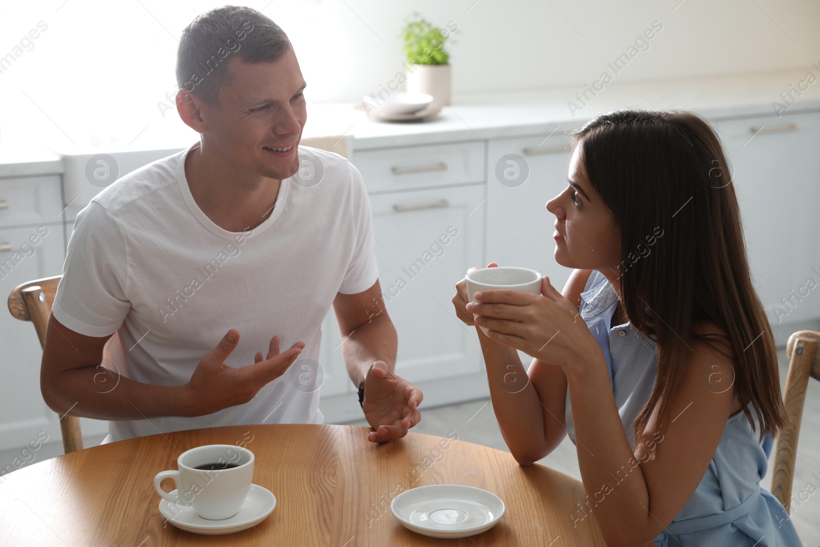 Photo of Man and woman talking while drinking tea at table in kitchen