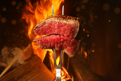 Image of Carving fork with pieces of beef steak near bonfire