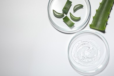 Photo of Petri dishes with cosmetic gel and cut aloe vera on white background, flat lay. Space for text