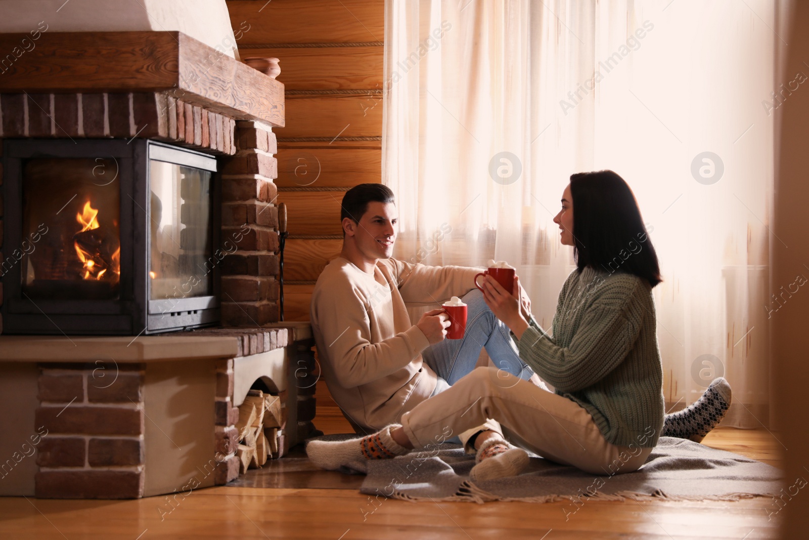 Photo of Lovely couple with delicious cocoa near fireplace on floor at home. Winter vacation