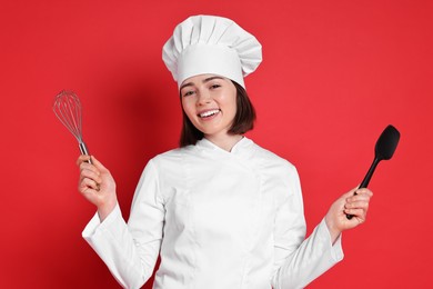 Happy confectioner holding whisk and spatula on red background