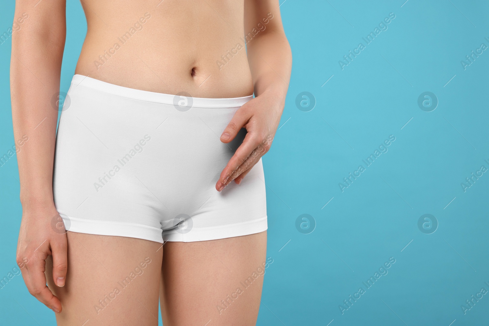 Photo of Woman holding hand near panties on light blue background, space for text. Women's health