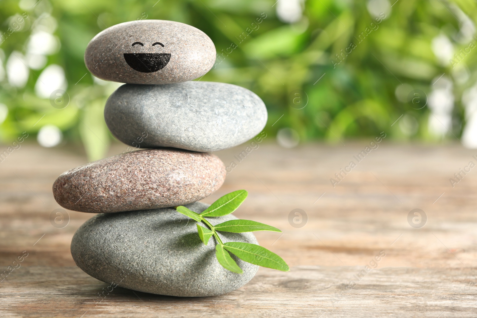 Image of Stack of stones with drawn happy face on wooden table, space for text. Be in harmony and enjoying your life