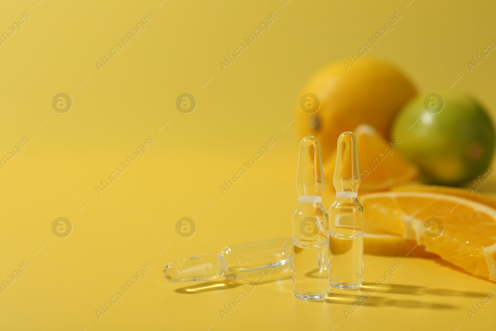 Photo of Skincare ampoules with vitamin C and citrus slices on yellow background, closeup. Space for text