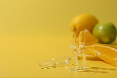 Skincare ampoules with vitamin C and citrus slices on yellow background, closeup. Space for text