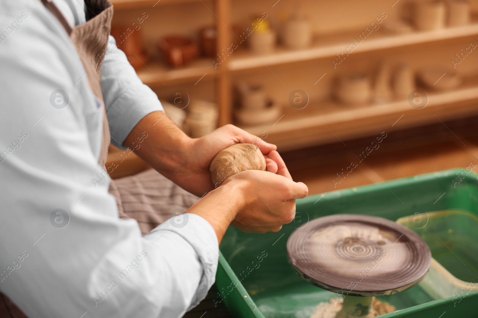 Photo of Man crafting with clay over potter's wheel indoors, closeup