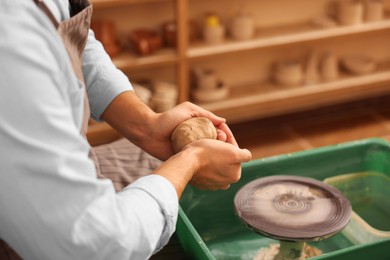 Man crafting with clay over potter's wheel indoors, closeup