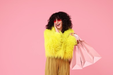 Photo of Happy young woman with shopping bags on pink background. Space for text