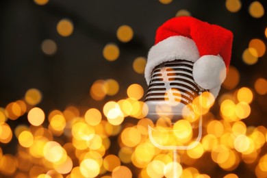 Christmas music. Microphone with Santa hat on black background, bokeh effect