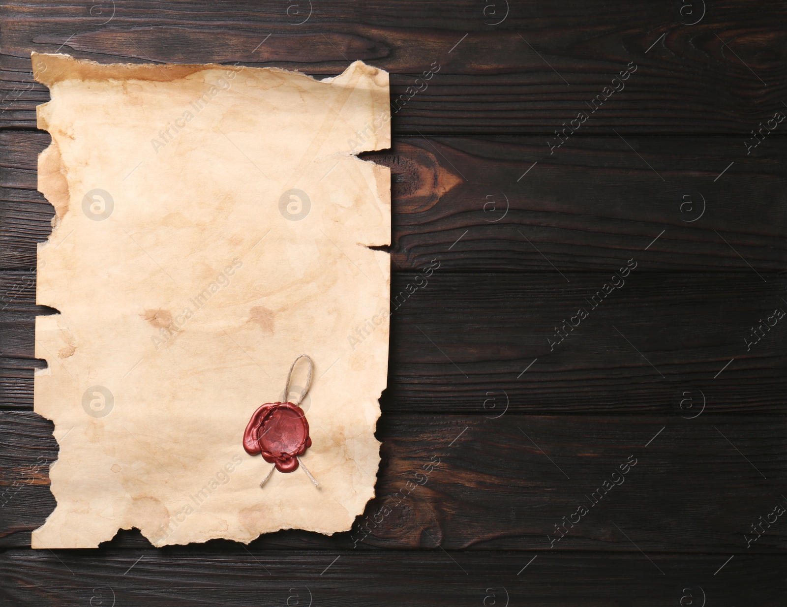 Photo of Sheet of old parchment paper with wax stamp on wooden table, top view. Space for text