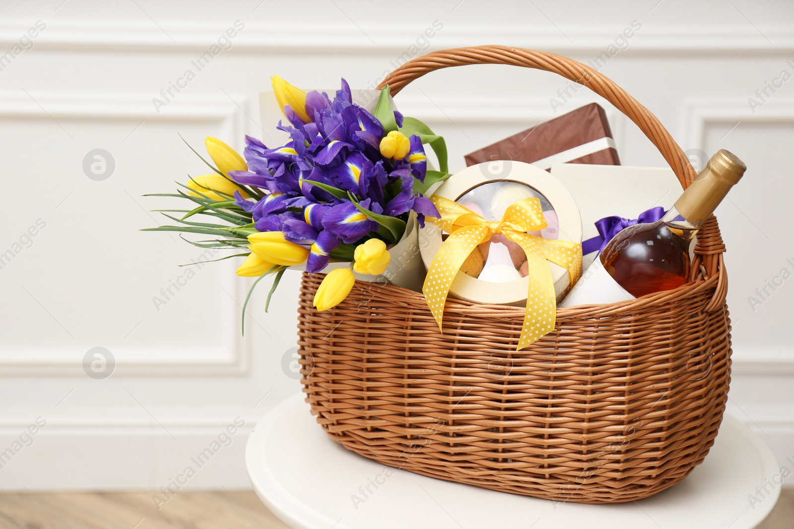 Photo of Wicker basket with gifts, bouquet and wine on white table indoors