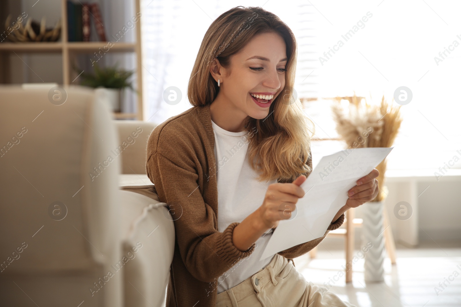 Photo of Happy woman reading letter near sofa at home