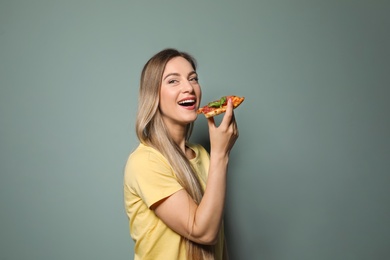 Photo of Attractive young woman with slice of delicious pizza on color background