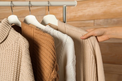 Photo of Woman choosing sweater on rack against wooden background