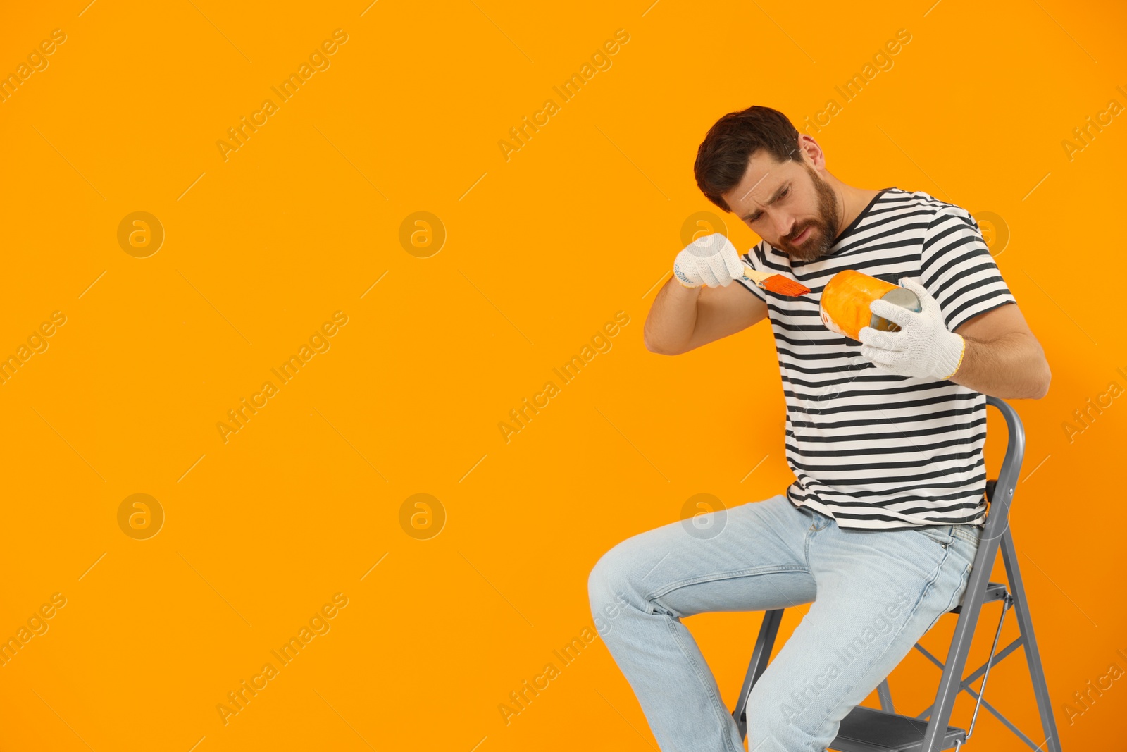 Photo of Designer with painting equipment sitting on folding ladder near freshly painted orange wall, space for text