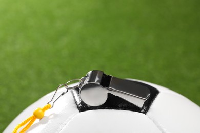 Photo of Football referee equipment. Soccer ball and metal whistle on green grass, closeup with space for text