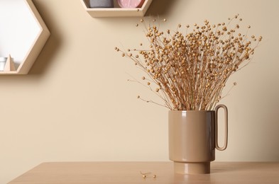 Photo of Stylish ceramic vase with dry flowers on wooden table near beige wall. Space for text