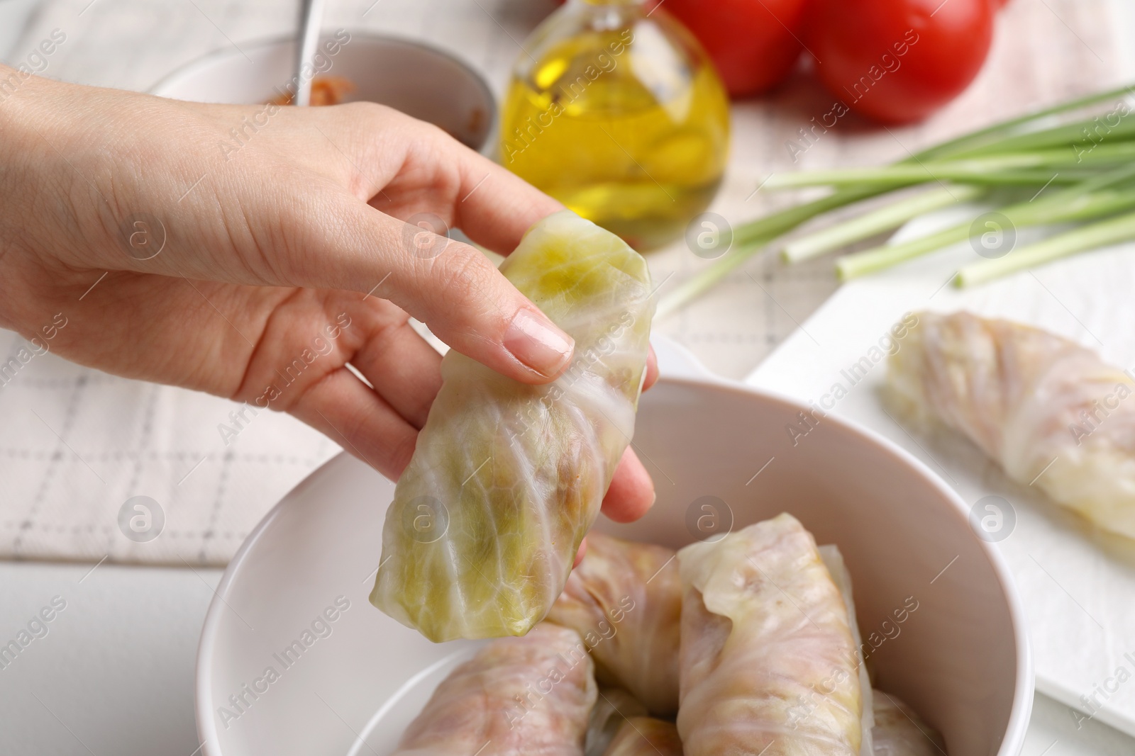 Photo of Woman putting uncooked stuffed cabbage roll into ceramic pot at table, closeup