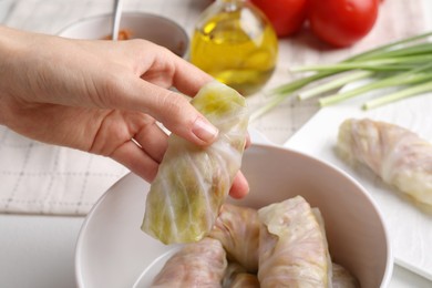 Woman putting uncooked stuffed cabbage roll into ceramic pot at table, closeup