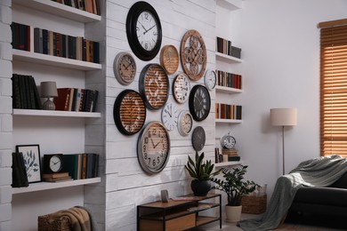 Stylish room interior with console table, comfortable sofa and collection of different clocks on white wall