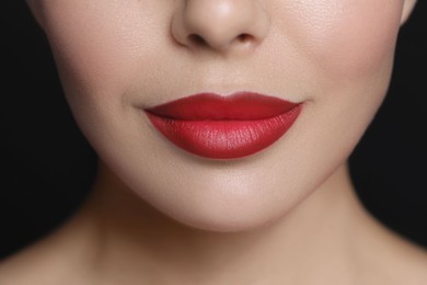 Photo of Young woman wearing beautiful red lipstick on black background, closeup