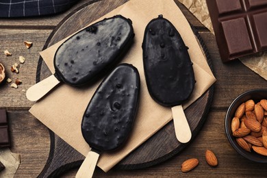 Delicious glazed ice cream bars, chocolate and nuts on wooden table, flat lay