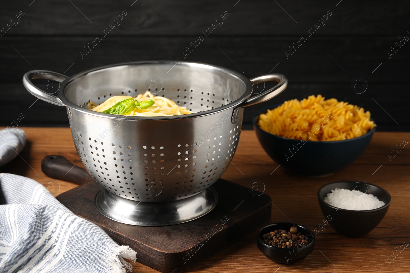 Photo of Cooked pasta in metal colander and spices on wooden table