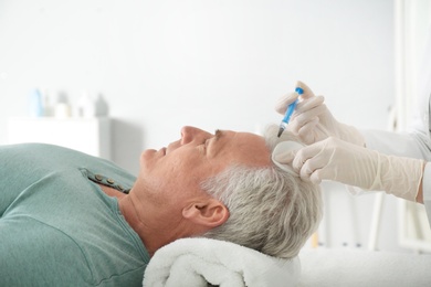 Senior man with hair loss problem receiving injection in salon