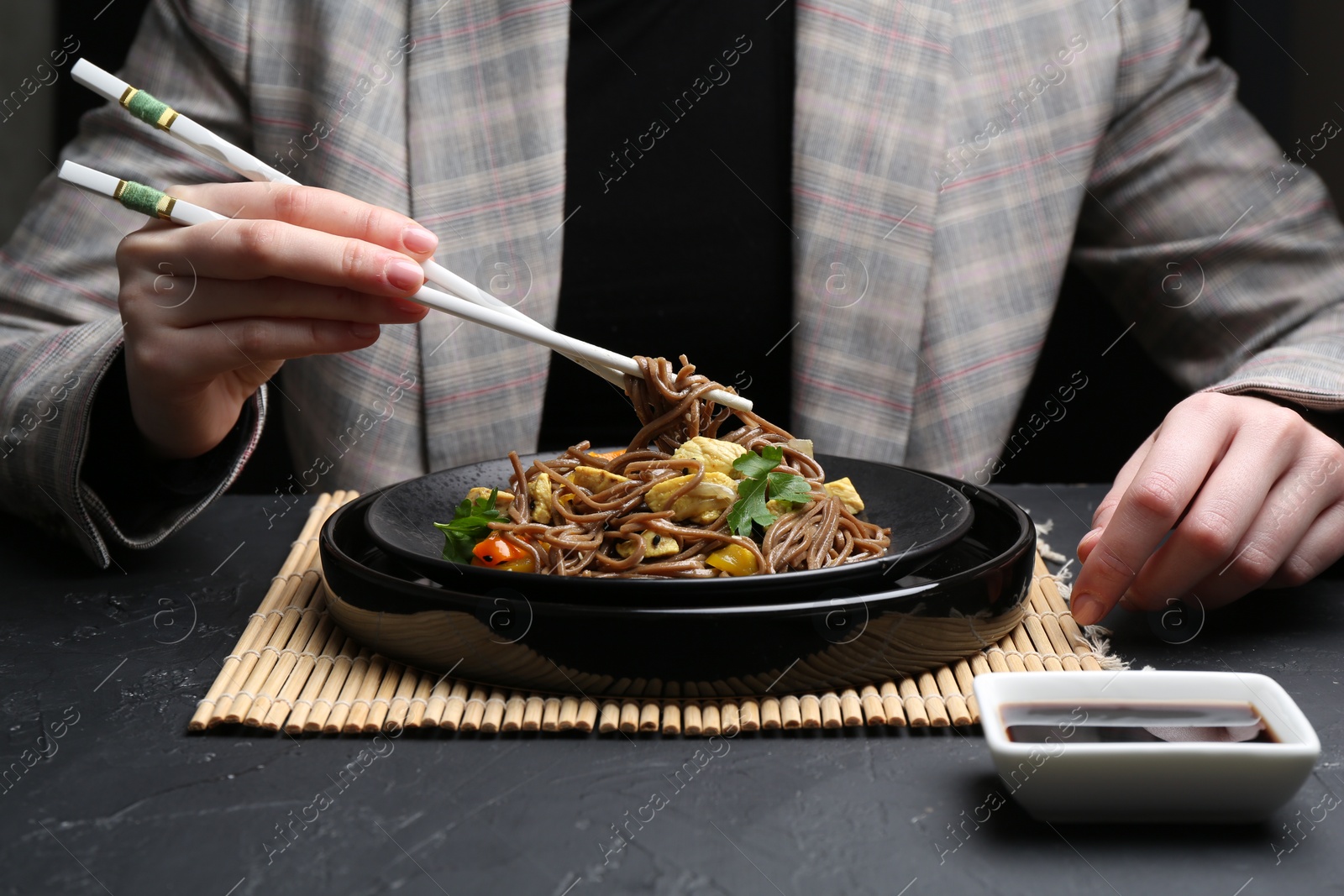 Photo of Stir-fry. Woman eating tasty noodles with meat and vegetables at dark textured table, closeup