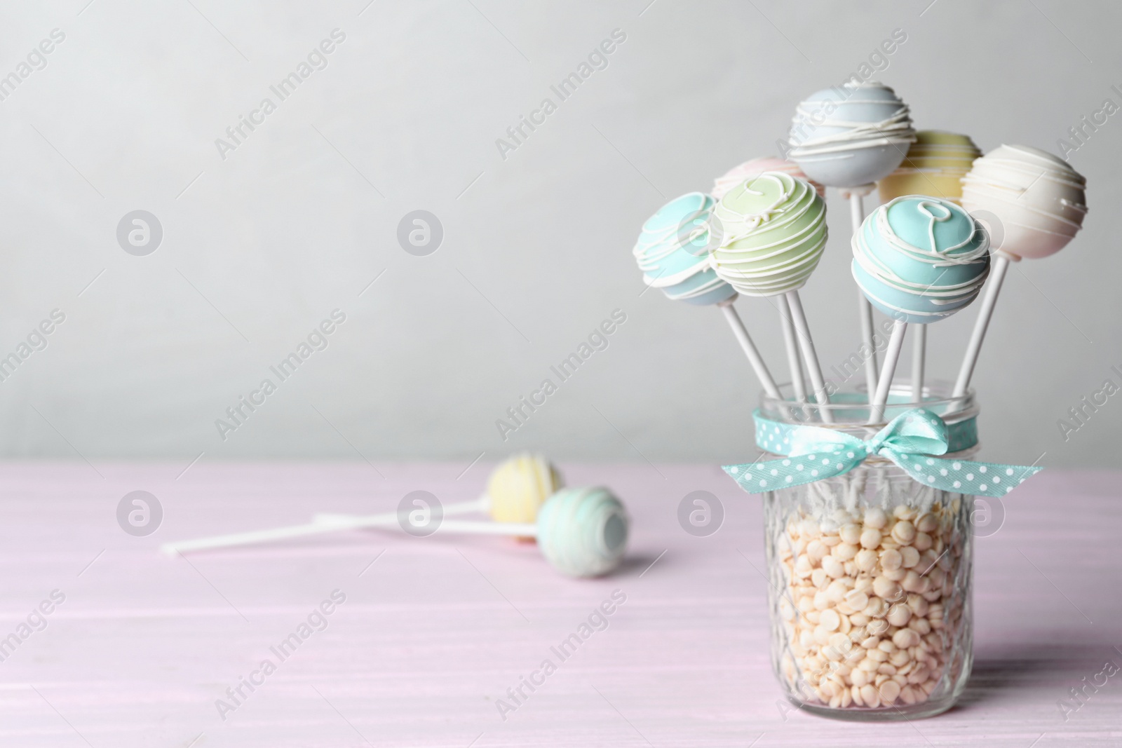 Photo of Sweet cake pops on pink wooden table against grey background. Space for text