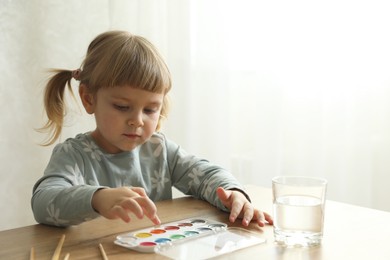 Photo of Cute little girl with supplies for drawing at wooden table indoors. Child`s art