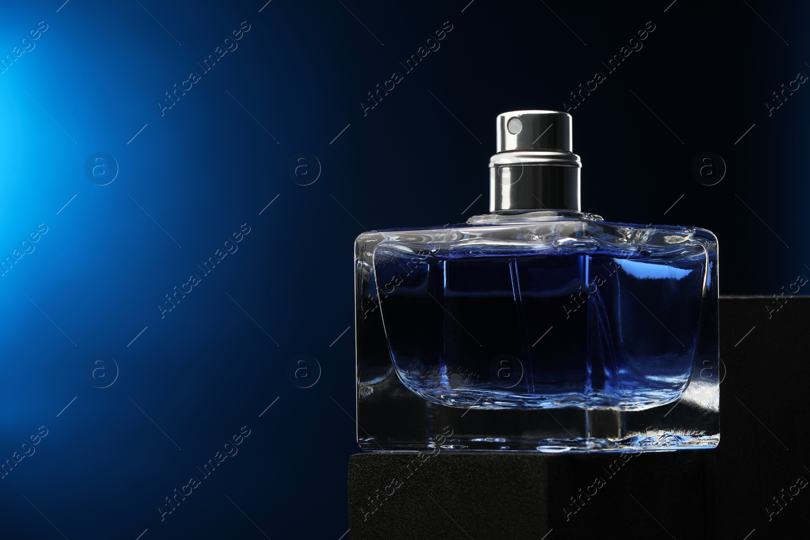 Photo of Luxury men`s perfume in bottle against dark blue background, space for text