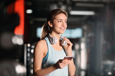 Photo of Young woman with headphones and mobile device at gym