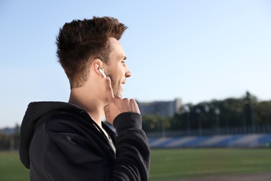 Young sportsman with wireless earphones at stadium