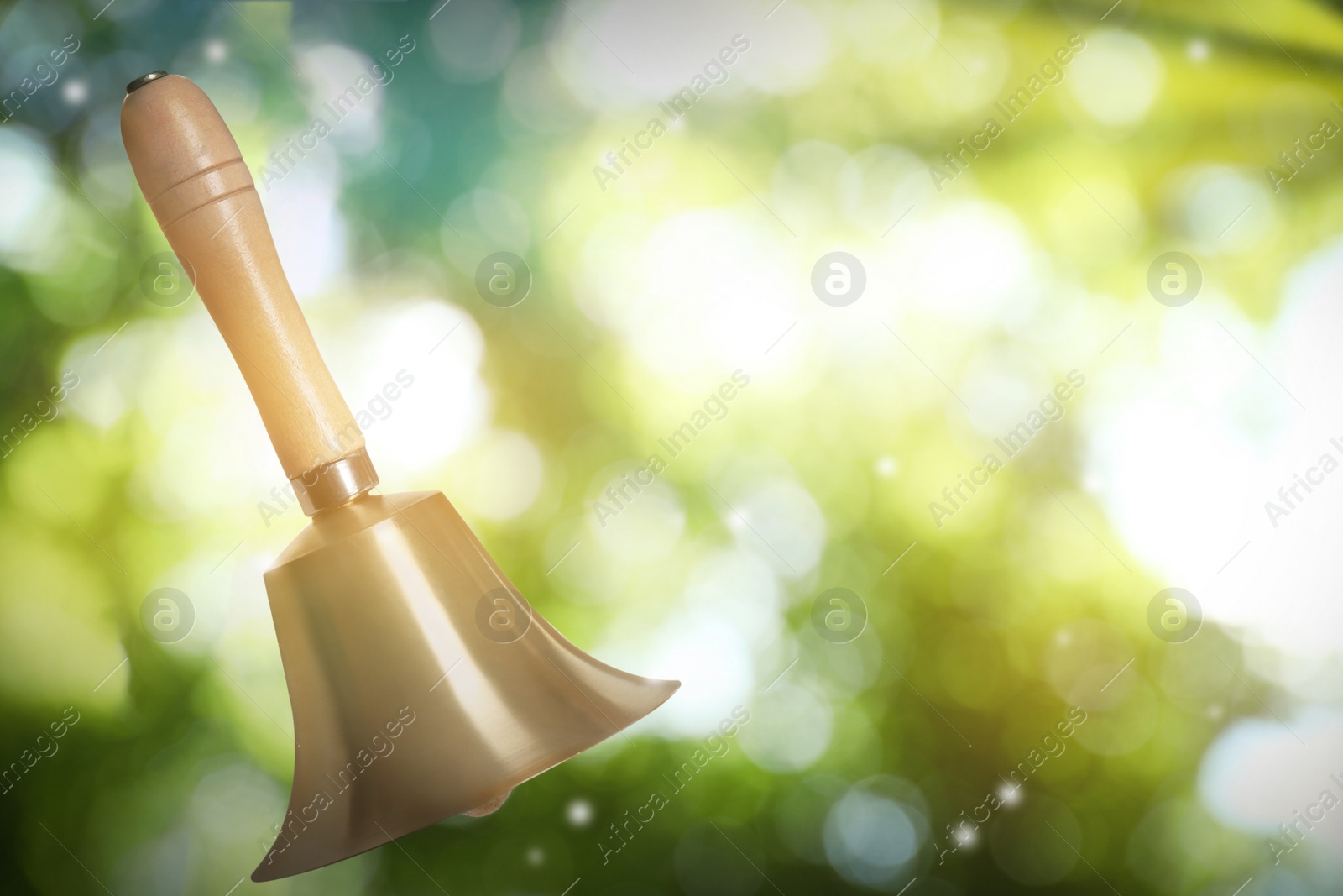 Image of Shiny school bell with wooden handle outdoors, space for text. Bokeh effect