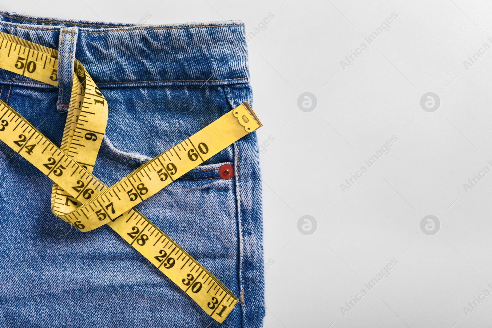 Photo of Jeans with measuring tape on light grey background, top view and space for text. Weight loss concept