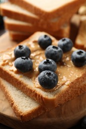 Photo of Delicious toasts with peanut butter and blueberries on wooden board, closeup