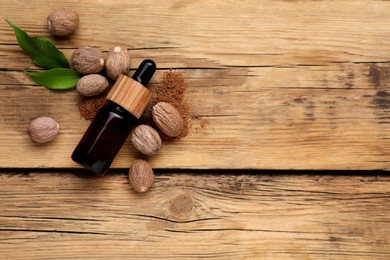 Photo of Bottle of nutmeg oil, nuts and powder on wooden table, flat lay. Space for text