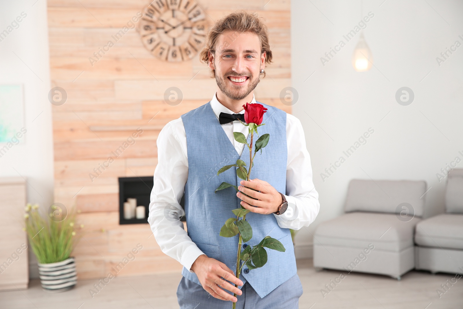 Photo of Handsome man in formal wear holding red rose indoors