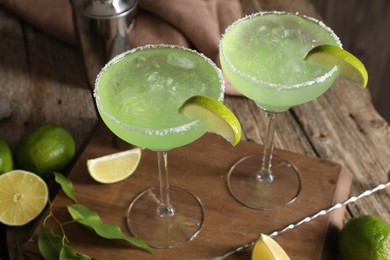 Photo of Delicious Margarita cocktail in glasses, limes and green leaves on wooden table