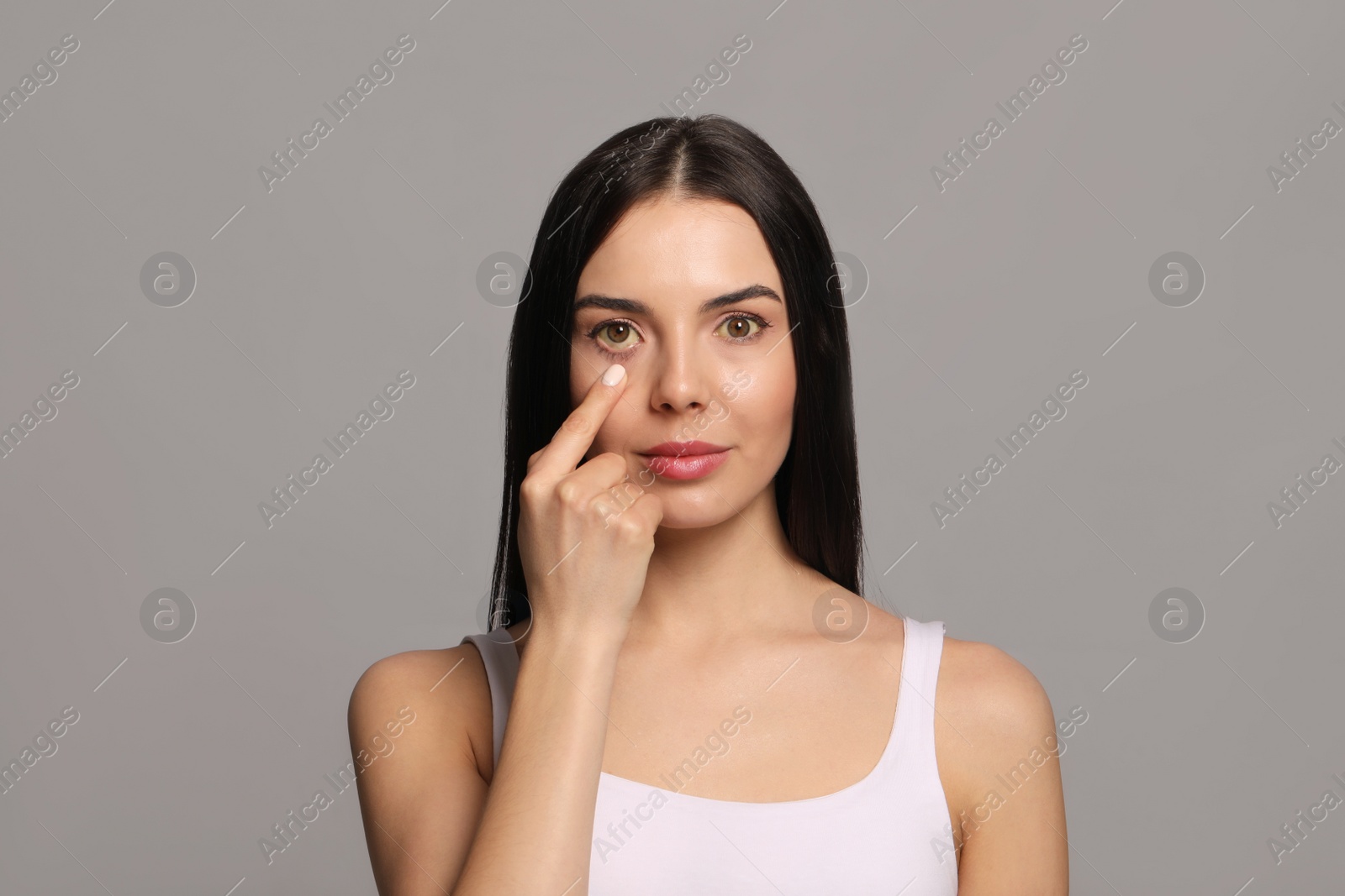 Photo of Woman checking her health condition on grey background. Yellow eyes as symptom of problems with liver