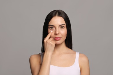 Woman checking her health condition on grey background. Yellow eyes as symptom of problems with liver