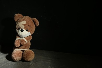 Photo of Stop child abuse. Tied toy bear with taped mouth and patches on grey floor against black background. Space for text