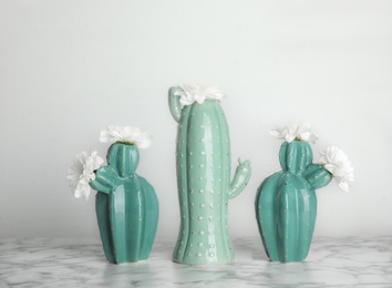 Photo of Trendy cactus shaped vases with flowers on table against light wall. Creative decor