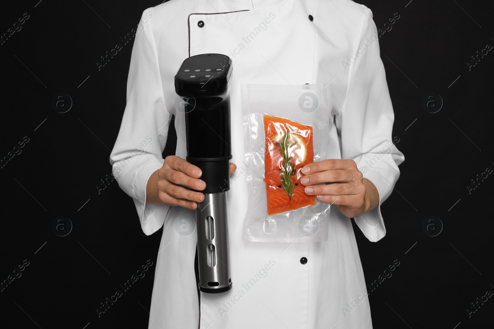 Photo of Chef holding sous vide cooker and salmon in vacuum pack on black background, closeup