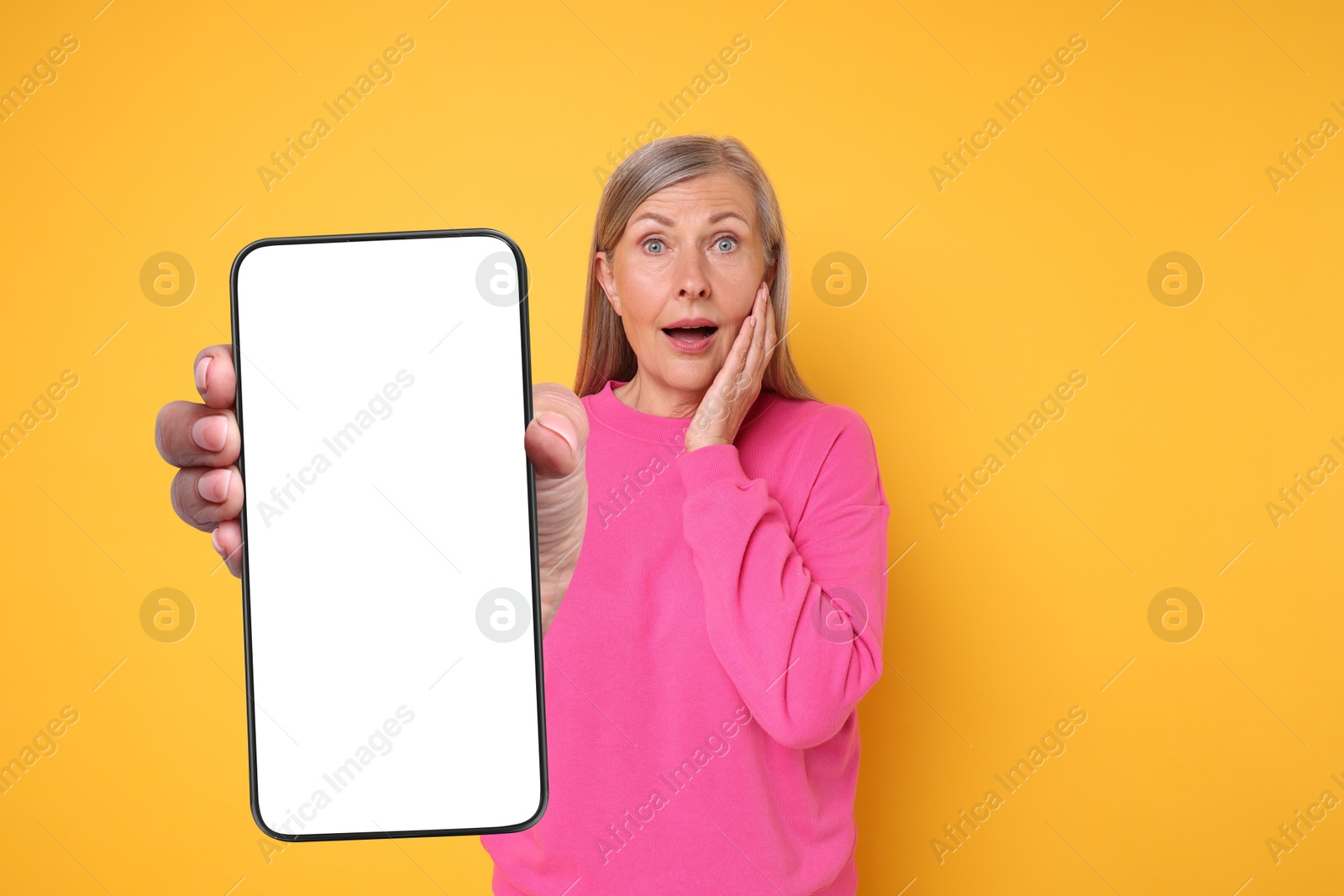 Image of Mature woman showing mobile phone with blank screen on golden background. Mockup for design